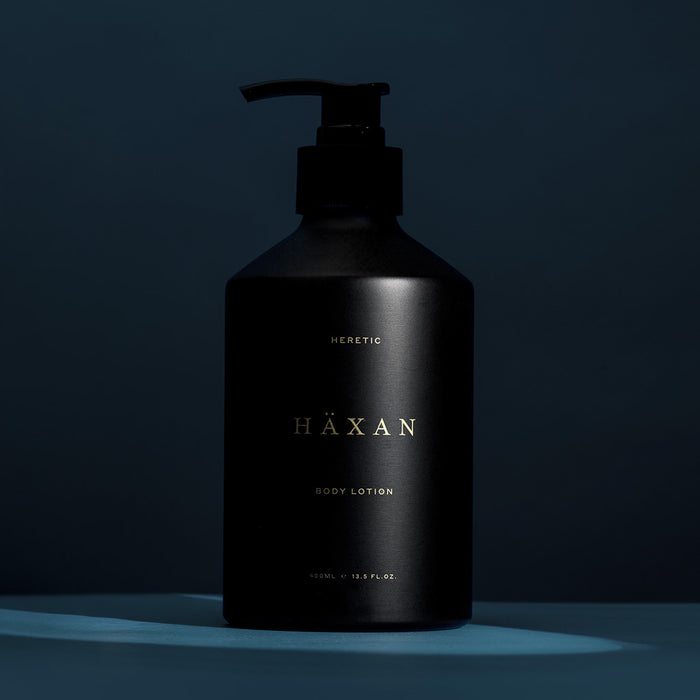 A matte black pump bottle of HÄXAN body lotion with gold lettering, set against a dark blue background with a cool-toned spotlight effect.
