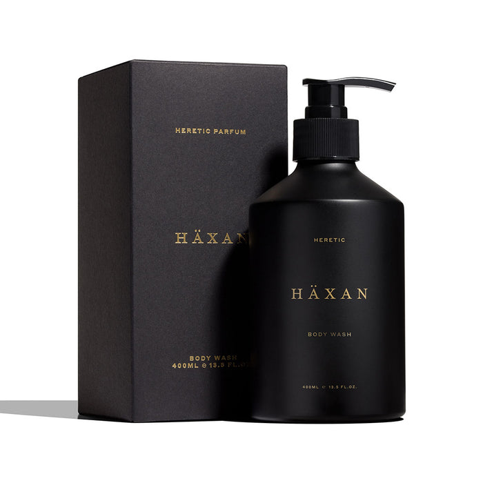 A matte black pump bottle of HÄXAN body wash by Heretic Parfum, standing next to its matching matte black box on a clean white background.