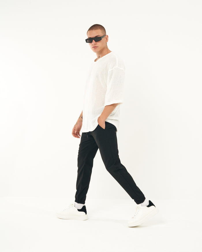 Martin Valen men's slim casual black jogger, three-quarter walking view with hand in pocket, elastic ankle and white sneakers
