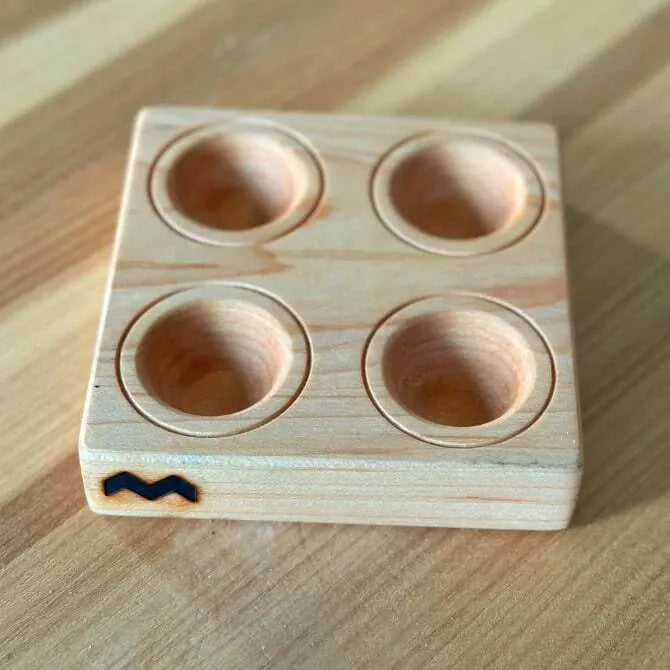 A square maple wood ravioli mold with 4 circular indentations, placed on a wooden surface.