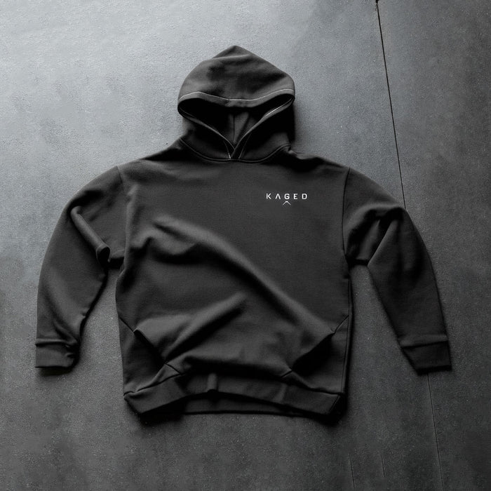 Front flat-lay of Ascent Hoodie showing white KAGED chest logo on black hoodie against dark textured background