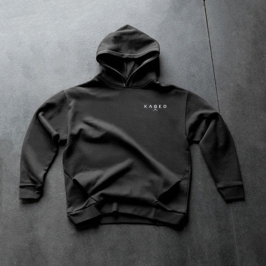 Front flat-lay of Ascent Hoodie showing white KAGED chest logo on black hoodie against dark textured background