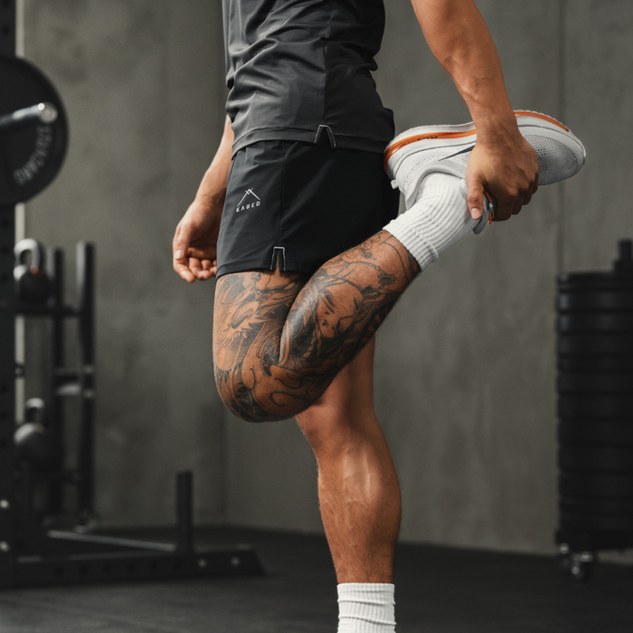 Side view of Ascent Performance Shorts showing black athletic fit, moisture-wicking 4-way stretch and KAGED logo in a gym