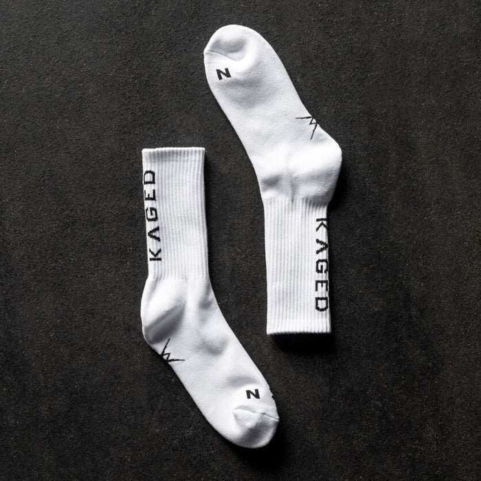 Top down view of Ascent Performance crew socks showcasing white ribbed cuffs and vertical KAGED logo on dark textured background
