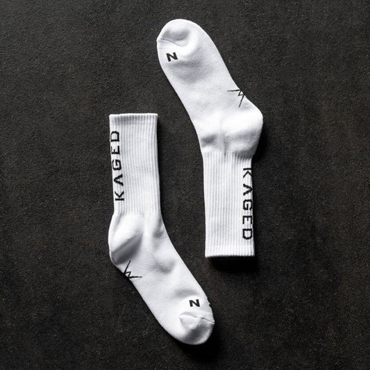 Top down view of Ascent Performance crew socks showcasing white ribbed cuffs and vertical KAGED logo on dark textured background