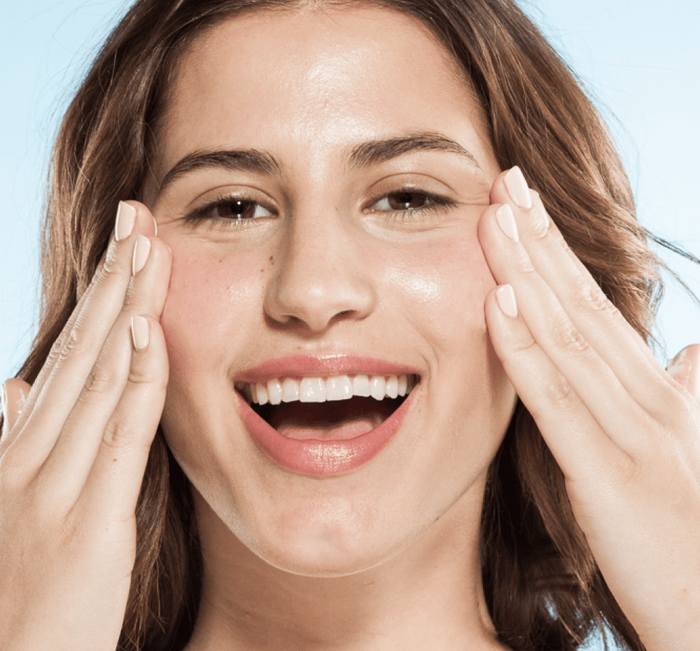 Smiling woman gently pressing her hands to her glowing face, illustrating fresh skincare results from using Chocolate Fig Vitamin Recovery Serum | Farmhouse Fresh.