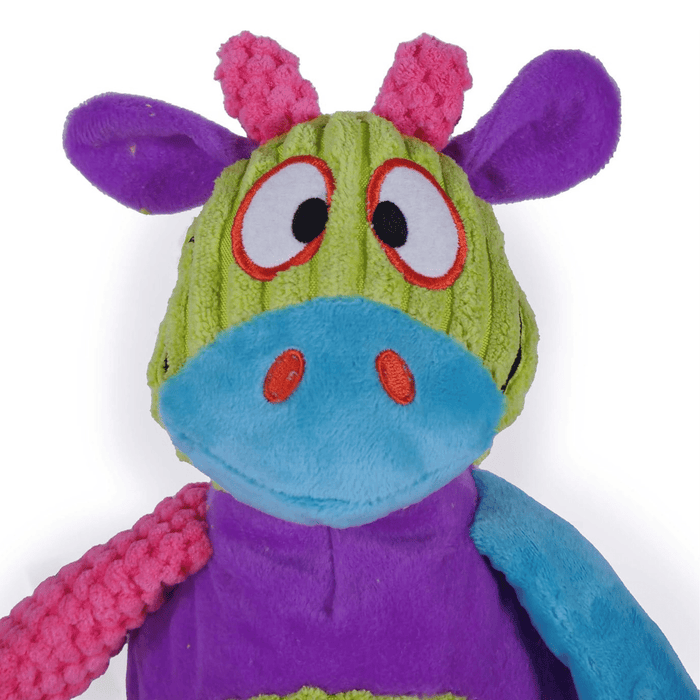 Close up of plush cartoon multi-coloured cow dog toy, patches of blue, green, purple and pink all over. Stitched eye, nostril and smile details on the face. Pictured on a white background.