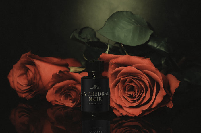 Perfume bottle labeled 'Cathedral Noir' surrounded by red roses on a dark background