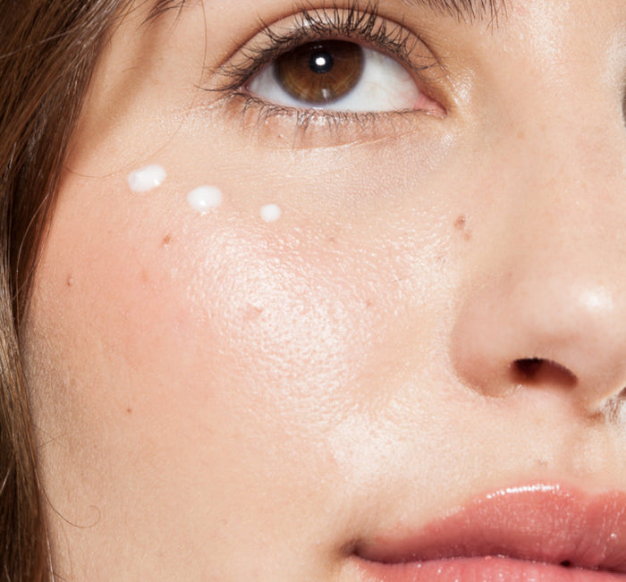 Close-up of a woman's face applying Crow Catcher® Eye Transforming Serum | Farmhouse Fresh in small dots under her eye, showcasing skincare application and smooth skin texture.