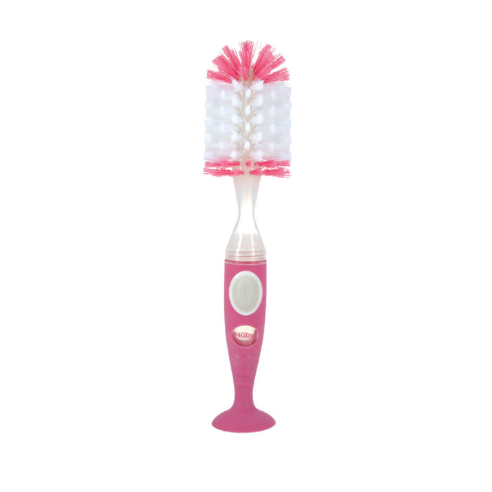 The Easy Clean Soap Dispensing Brush with Suction Base features a pink and white design, wide bristled head, textured handle, and suction base for stable cleaning of baby bottles.