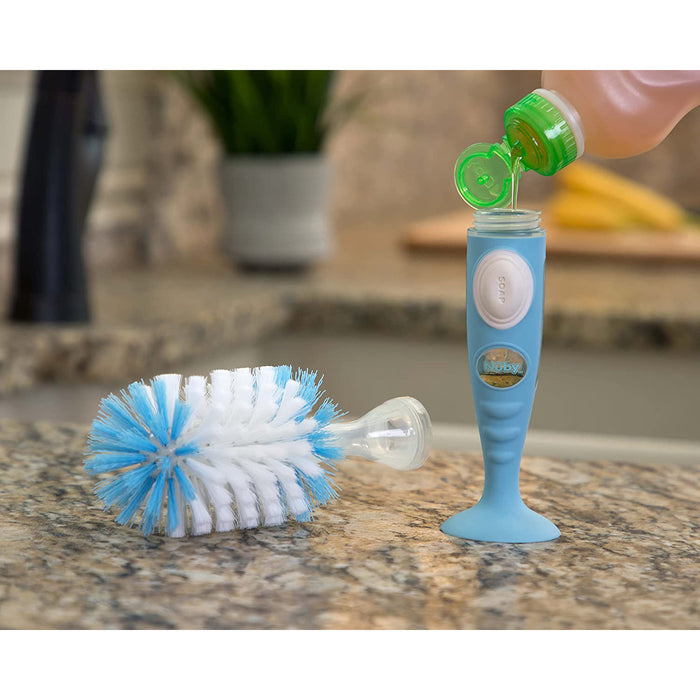 A hand fills the Easy Clean Soap Dispensing Brush with Suction Base using dish soap; its built-in dispenser releases soap during cleaning, making kitchen tasks more convenient. The brush rests on a granite counter.