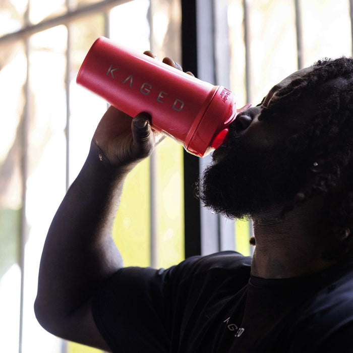 Person drinking from red Elite Strada insulated shaker bottle by a sunlit window