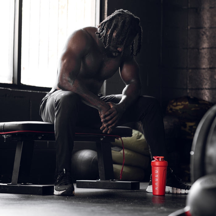 Athlete resting on a weight bench with a red KAGED Strada shaker bottle on the gym floor