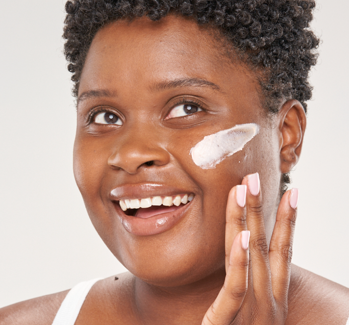 Woman smiling while applying Evening Rose Moon Dip® Ageless Facial Sleep Mousse with Peptides + Retinol | Farmhouse Fresh to her cheek as part of a skincare routine.