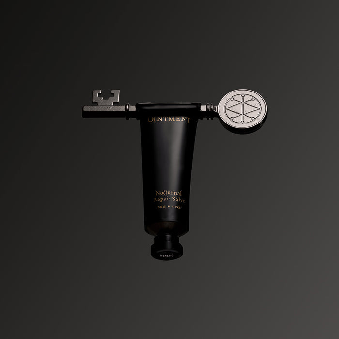 A black Flying Ointment Salve tube centered against a dark gray gradient background. Extending from the top of the tube is a metallic key-shaped applicator.