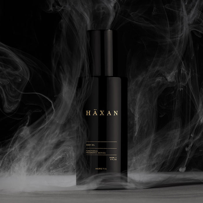 HÄXAN body oil bottle stands centered against a dark background with swirling smoke effects.