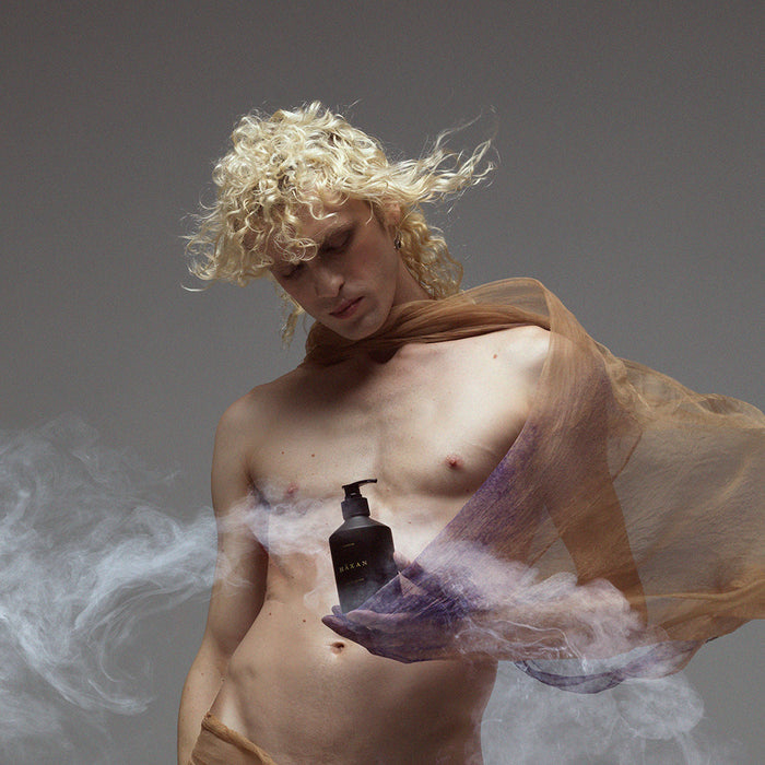 Ethereal model holding body wash, surrounded by curls of fog.