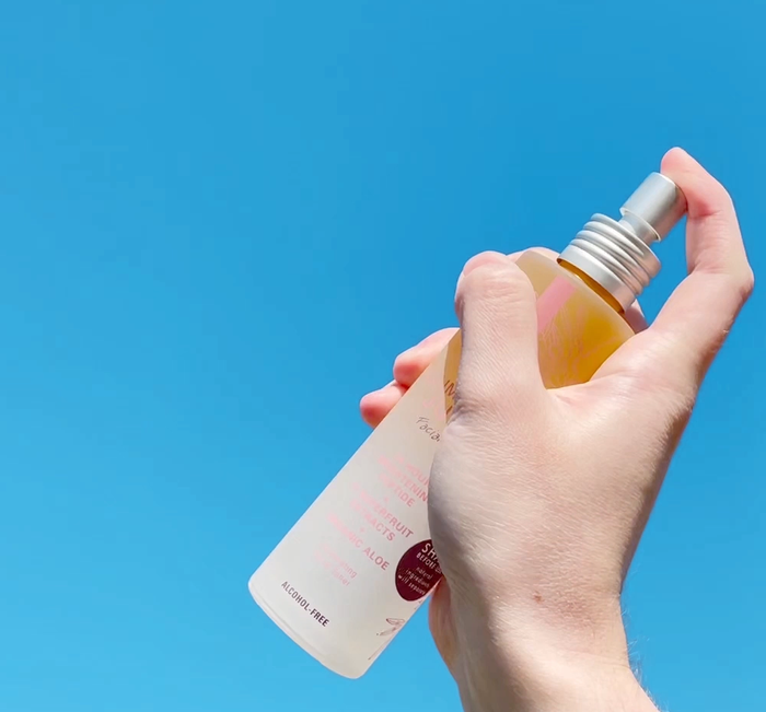 Hand holding a translucent spray bottle of Illumination Juice® Facial Tonic – Illuminating Facial Toner | Farmhouse Fresh against a bright blue background, highlighting skincare and wellness.