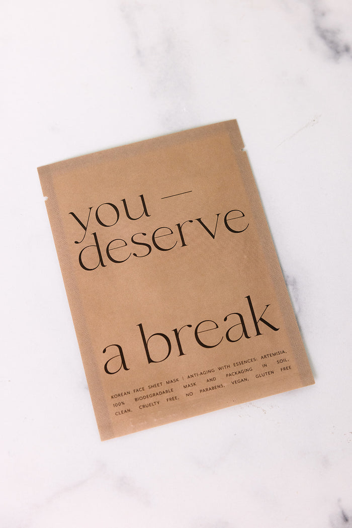 Brown biodegradable packaging of Korean Sheet Mask - You Deserve a Break | Lucky Owl on a white marble surface, featuring minimalist black text and eco-friendly skincare branding.