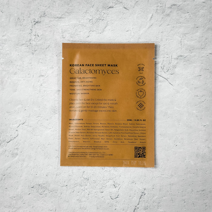 A brown packaging pouch for Korean Sheet Mask - You've Got This | Lucky Owl, featuring text about brightening and anti-aging benefits, placed on a light textured surface.
