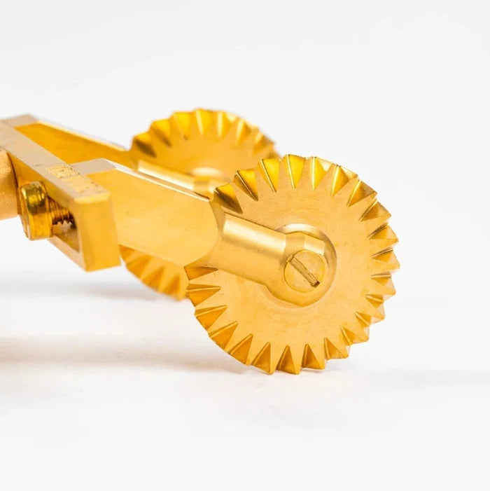 closeup of Gold pasta cutter on a white background.
