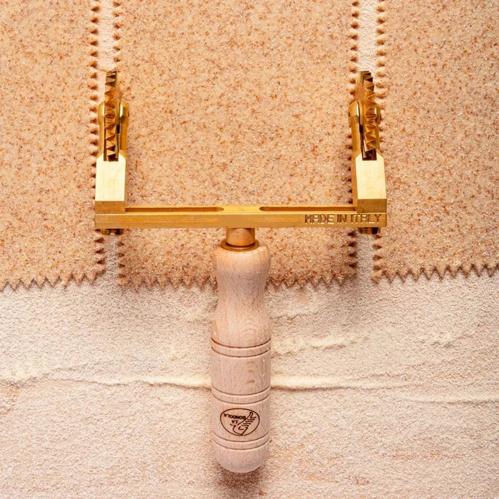 Pasta cutter with gold heads and wooden handles on a textured beige background