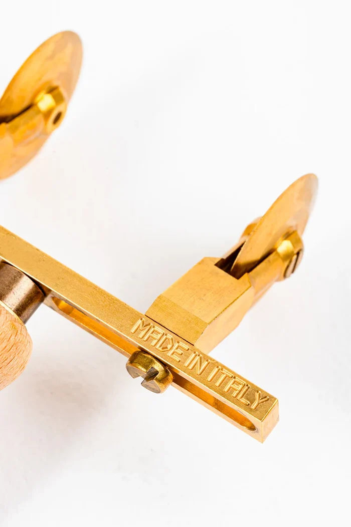 A professional adjustable ravioli cutter with two smooth wheels made of brass and a natural wood handle showing "Made in Italy" on brass cutter on white background.