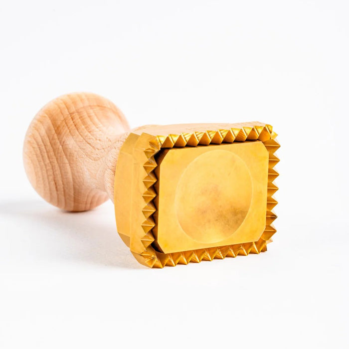 A rectangular brass pasta stamp with a wooden handle, featuring the text 'LA GONDELA' on the stamp surface on its side on a white background.
