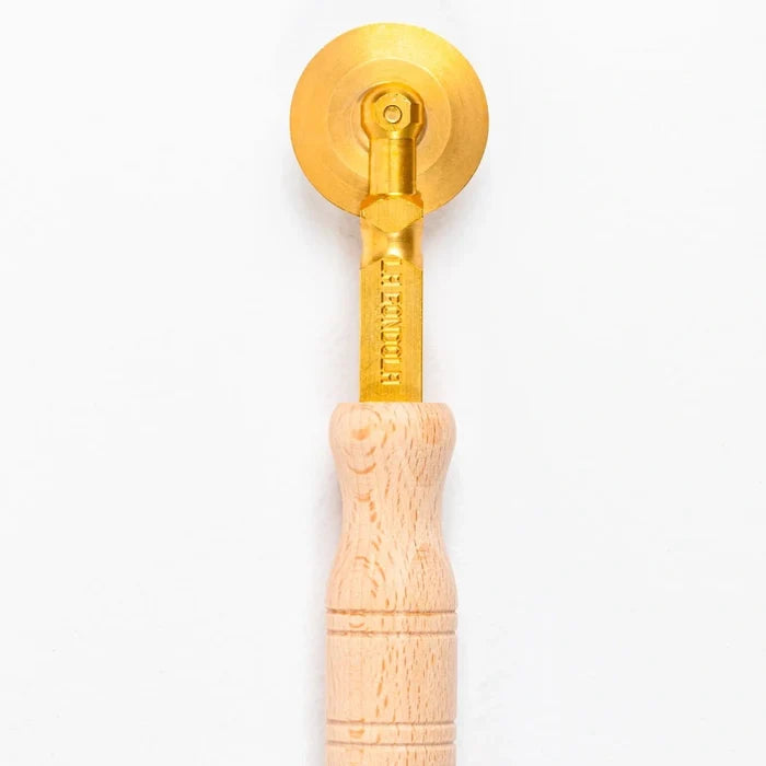 Wooden pasta cutter with gold wheel on a white background.