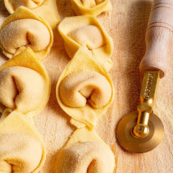 Handmade pasta with a gold pasta wheel on a wooden surface
