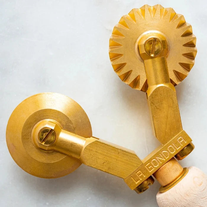 Closeup of handmade brass pasta cutter with a smooth and fluted wheel, featuring a wooden handle.