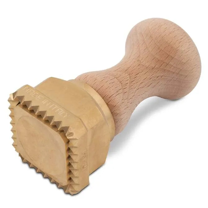 A square-shaped pasta stamp with a brass base and a wooden handle, 45 mm in size on its side on a white background.