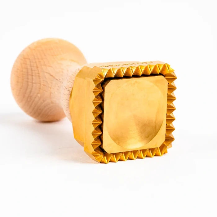 A square-shaped pasta stamp with a brass base and a wooden handle, 45 mm in size, highlighting the brass stamp on its side on a white background.