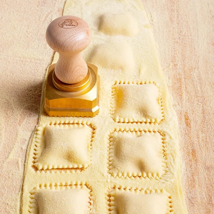 Wooden pasta stamp pressing square pasta patterns into dough on a wooden surface.