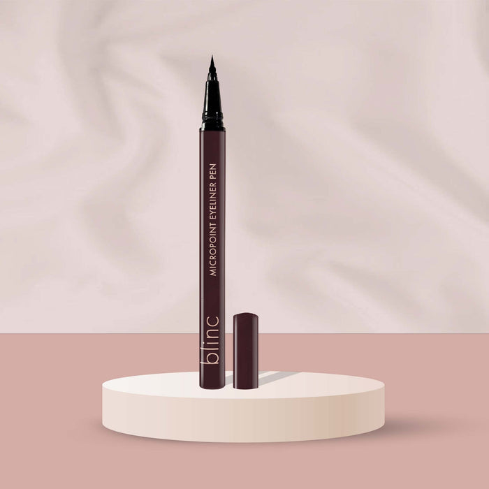 Micropoint Liquid Liner Pen | Blinc standing upright on a round pedestal with the cap removed, showcasing its fine precision tip against a soft beige and pink background.