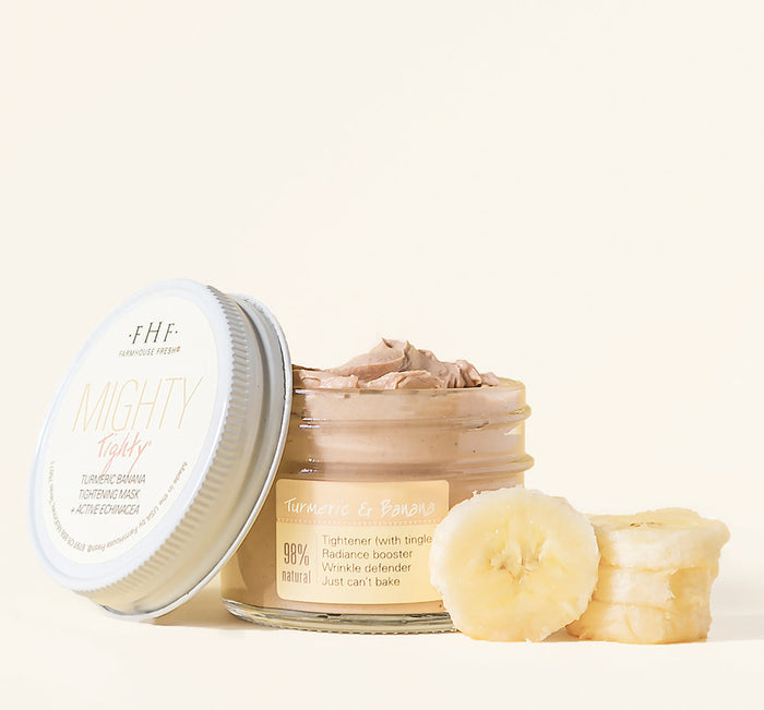 Open jar of Mighty Tighty® Turmeric & Banana Tightening Mask | Farmhouse Fresh with creamy texture beside fresh banana slices on light background, suggesting natural skincare.