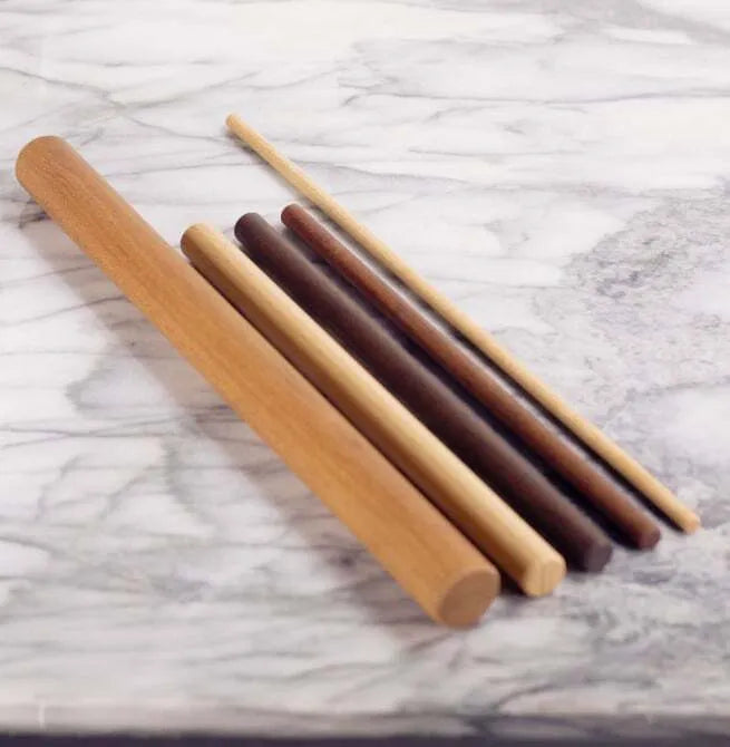 A set of wooden mini rolling pins of varying sizes laid out on a marble surface.