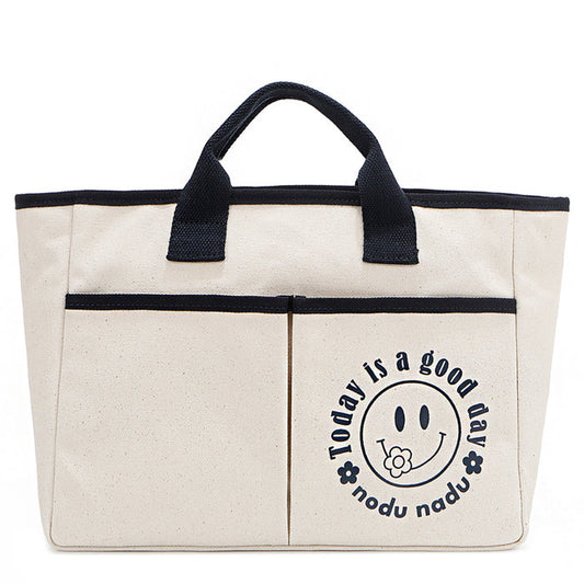 Your daily dose of positivity—now in bag form! With sleek trim details and a feel-good message, this everyday tote is here to remind you that yes, today (and every day) is a good one. Designed for both style and function, it features plenty of compartments inside like 2 front slip pockets. Pictured in classic, canvas-colored beige front angle view for a timeless statement that compliments any look from day to night! Smiley face adorns the front with a cute little flower on its smile.