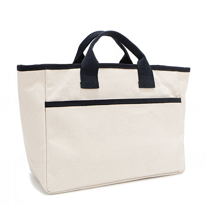 Back angle of the Emery handbag by Nodu Nadu in classic canvas-beige with navy blue trim. Dual top handles and a convenient black slip pocket to keep most-used items like your phone, keys, and planner close at hand.
