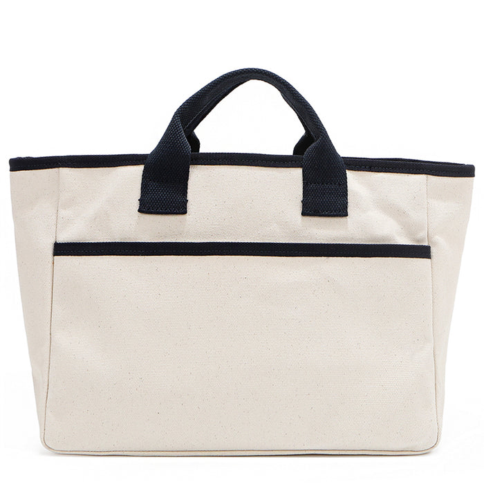 Back angle of the Emery handbag by Nodu Nadu in classic canvas-beige with navy blue trim. Made of polyester with dual top handles and a convenient black slip pocket to keep most-used items like your phone, keys, and planner close at hand. Dual top handles with a 3" drop allow you to carry this handbag by the top handles.