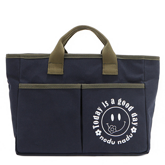 Your daily dose of positivity—now in bag form! With sleek trim details and a feel-good message, this everyday tote is here to remind you that yes, today (and every day) is a good one. Designed for both style and function, it features plenty of compartments like 2 front slip pockets. Pictured in classic navy blue with moss green trim and straps. White smiley face adorns the front with a cute little flower on its smile.
