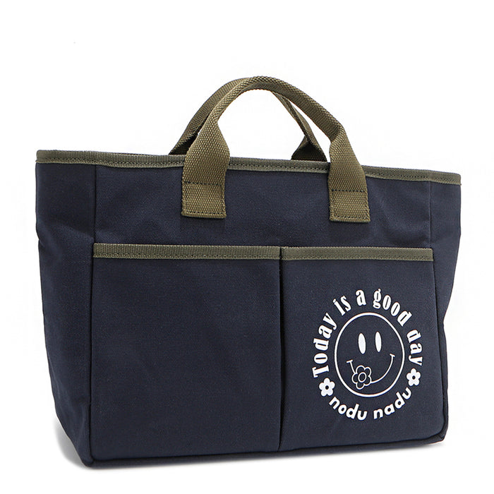 With sleek trim details and a feel-good message, this everyday tote is here to remind you that yes, today (and every day) is a good one. Designed for both style and function, it features plenty of compartments like 2 front slip pockets. Front angle pictured in classic navy blue with moss green trim and straps. White smiley face adorns the front with a cute little flower on its smile in this rectangular silhouette.