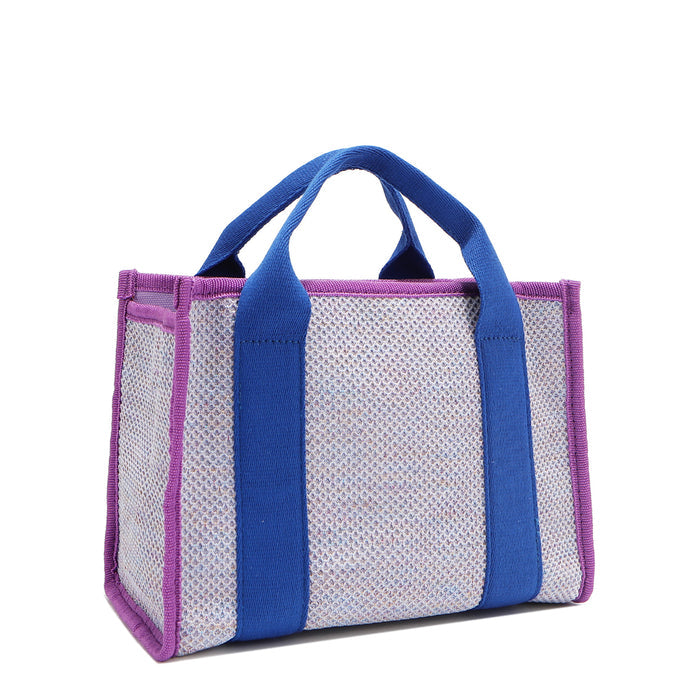 Back angle view of the Nodu Nadu small canvas Marley tote Bag in lavender. Accented with bold electric blue straps and a gorgeous purple trim, this canvas features a subtle metallic shimmer that hits the light whenever you walk for a head-turning detail.