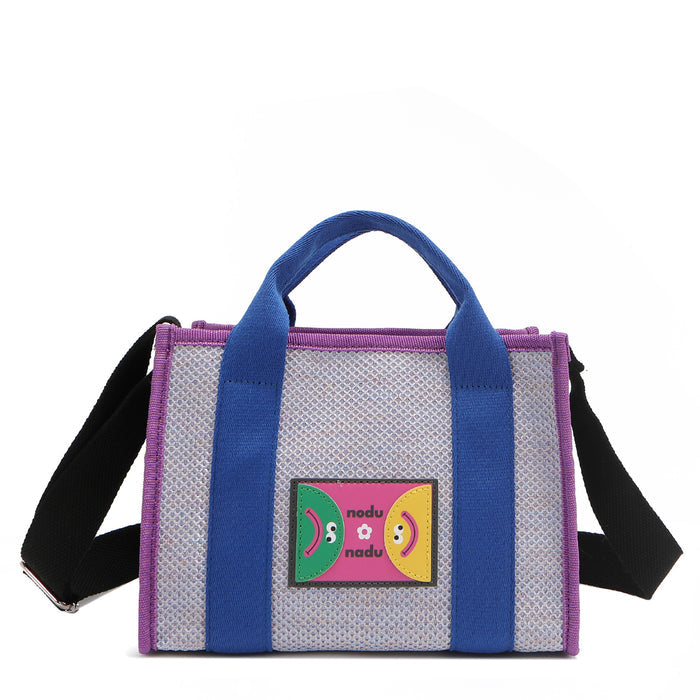 Front view of Nodu Nadu Marley Bag in Lavender with optional, adjustable and detachable black wide shoulder strap attached to show varied carrying options. Wear this rectangular tote by the top handles or around the shoulder or across the body!