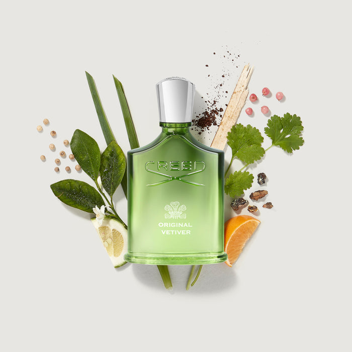 Creed Original Vetiver Bottle Surrounded by Fresh Vetiver, Citrus and Pepper Notes - Ingredient Flat Lay | Creed Fragrances