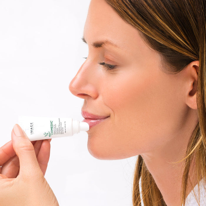 Woman applying ORMEDIC lip enhancement complex | IMAGE Skincare lip treatment to her lips, demonstrating skincare and wellness care.