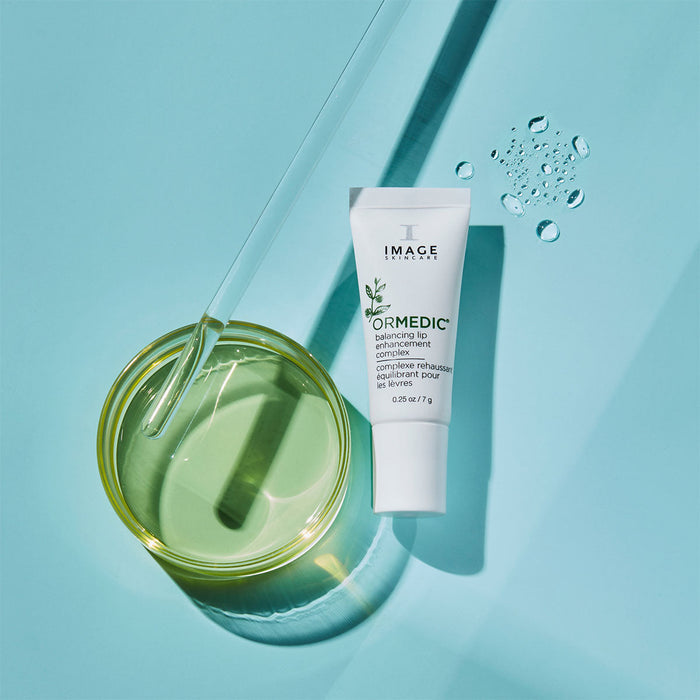 ORMEDIC lip enhancement complex | IMAGE Skincare tube next to a small glass dish with green liquid and a dropper, highlighting skincare and wellness product features.