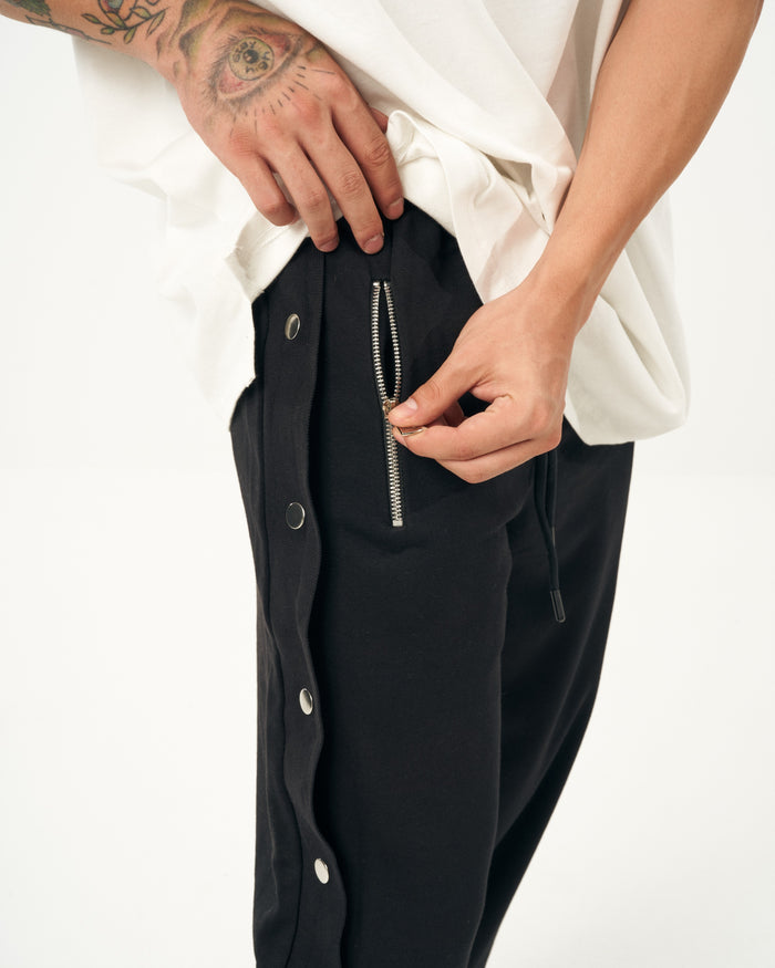 Martin Valen oversized black baggy jogger, close-up of hand fastening the metal zipper and side press stud