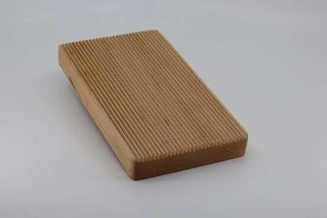Wooden pasta board with ridges on white background.
