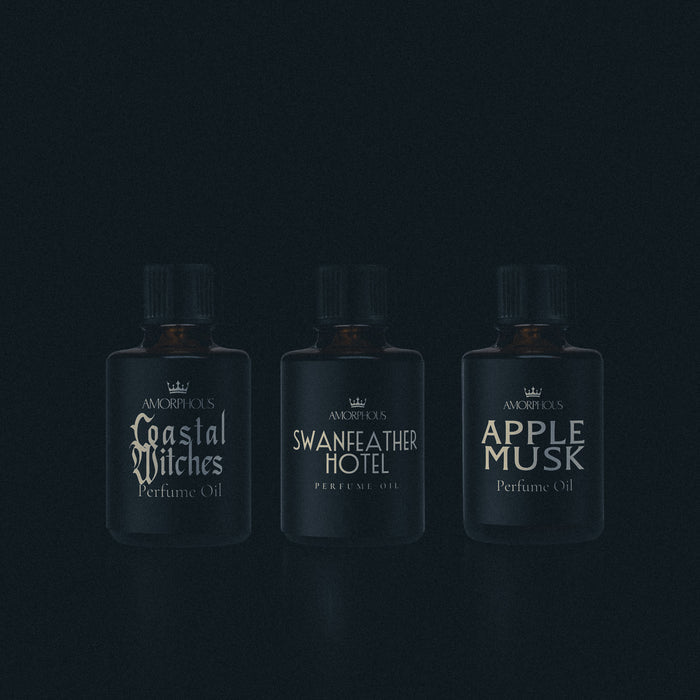 Three perfume bottles labeled 'Coastal Witches', 'Swanfeather Hotel', and 'Apple Musk' on a dark background.